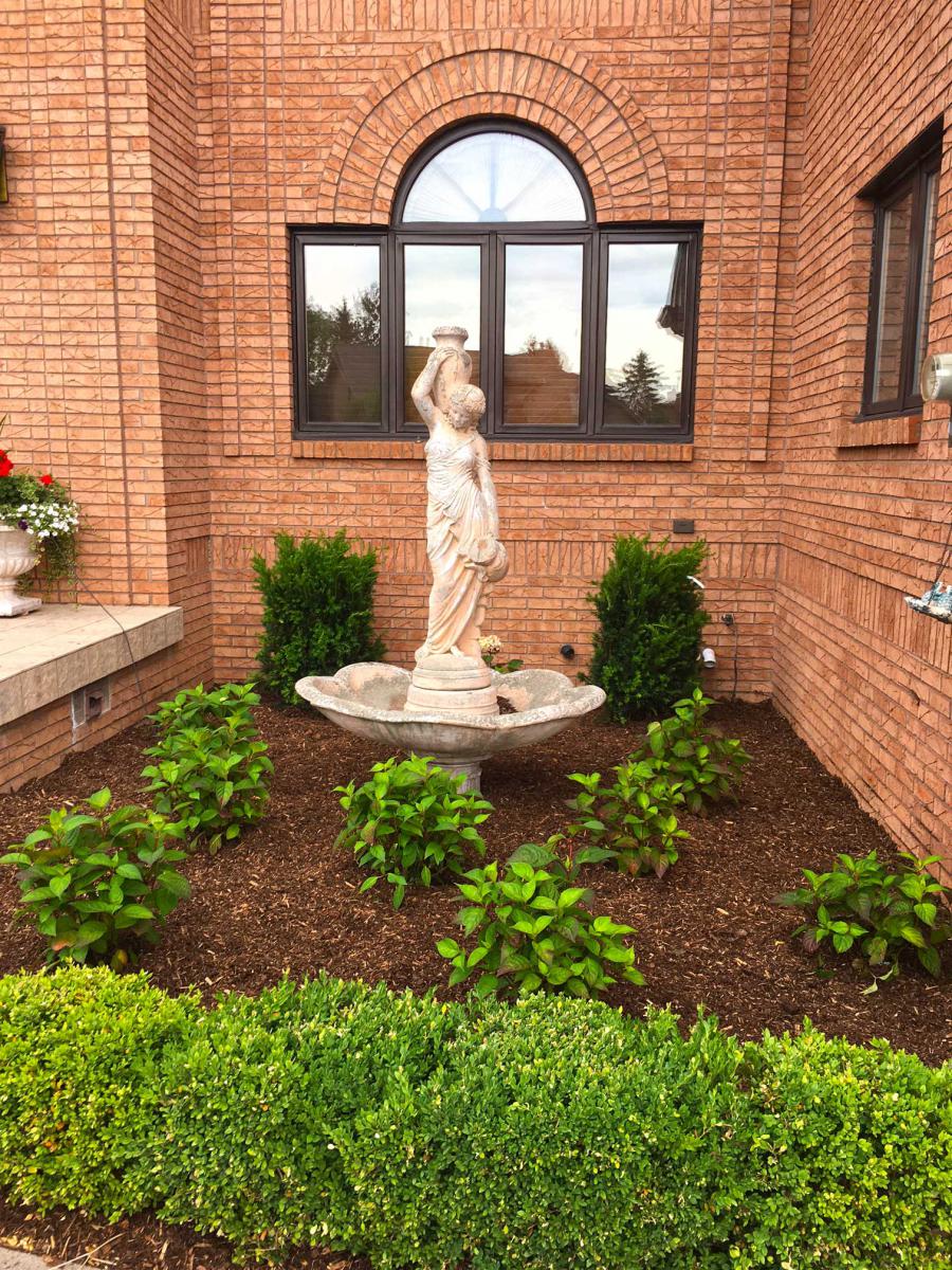 Shrub landscaping work done around outdoor statue.